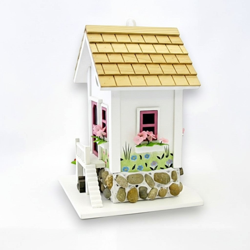 Mellow Monkey May Cottage birdhouse with white exterior, pink window frames, flower boxes, stone base, and wooden shingle roof.