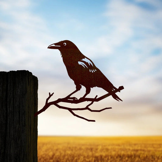 Mellow Monkey MetalBird crow silhouette garden art made of mild steel, mounted on a wooden post against a sunset sky.