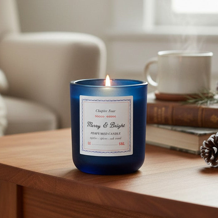 Mellow Monkey Merry & Bright scented candle in a midnight blue glass jar on a wooden table with books and pinecones.