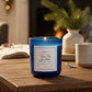 Mellow Monkey And to All a Good Night candle in a midnight blue glass jar on a wooden table by a cozy fireplace.
