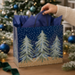 Mellow Monkey large gift bag with midnight snowfall and pine tree print, featuring blue tissue paper and handles.
