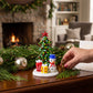 Mellow Monkey Milano art glass Christmas tree figurine with a snowman and gifts on a festive holiday table setting.