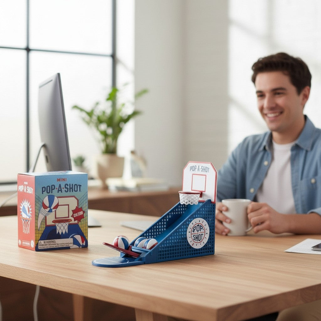 Mellow Monkey Mini Pop-A-Shot desktop basketball game with mini balls and box on an office desk with a man smiling