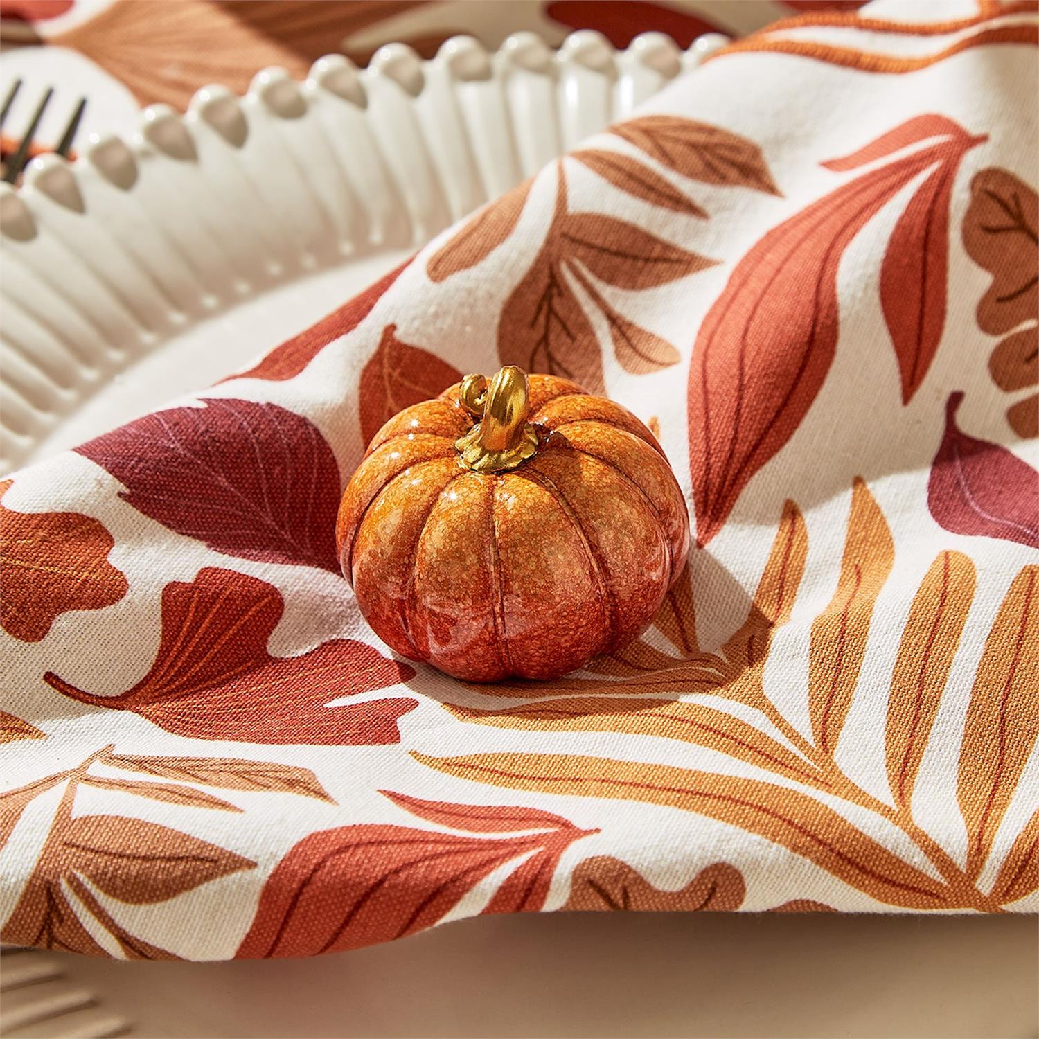 Mellow Monkey hand-painted mini resin pumpkin in orange and gold sitting on a fall-themed leaf print napkin
