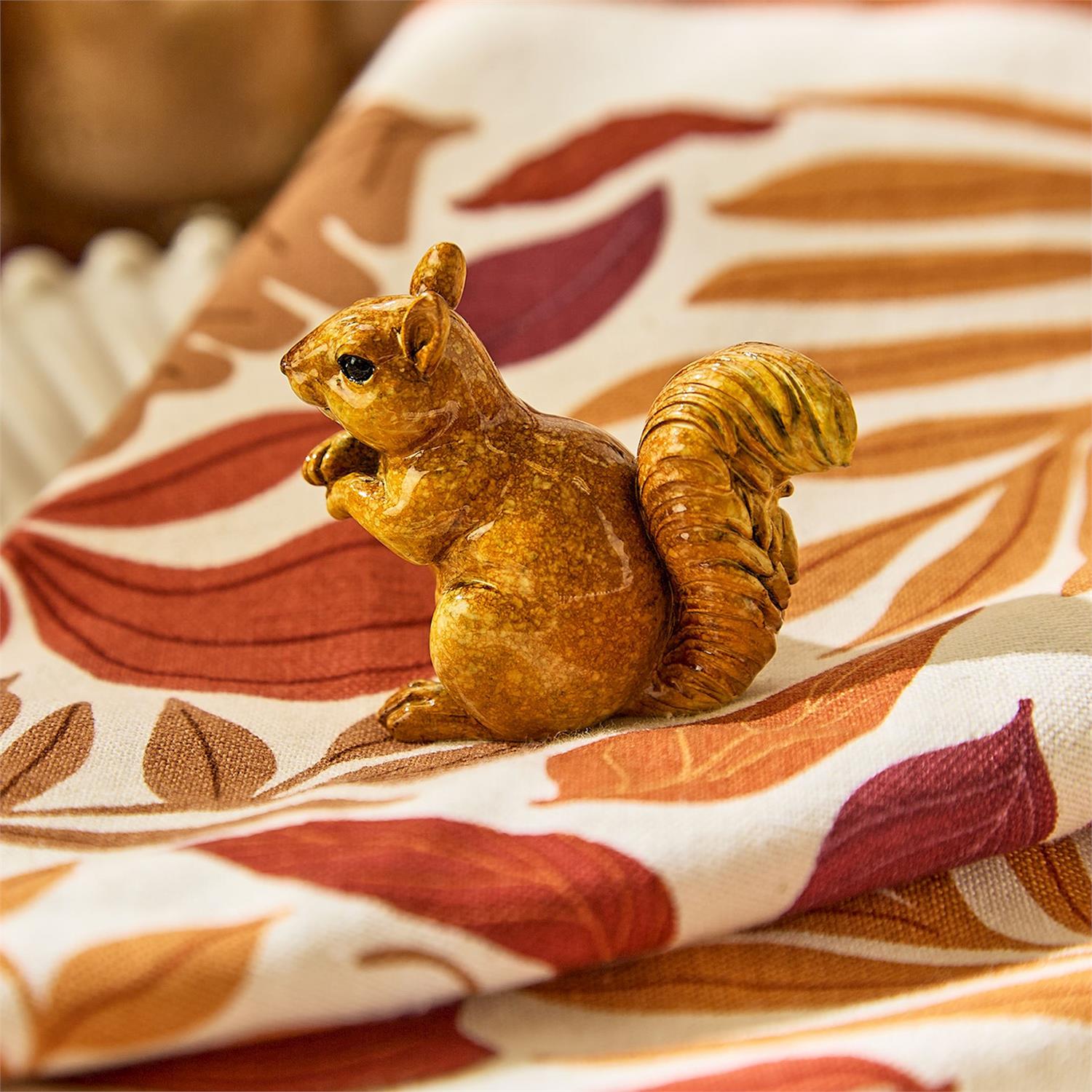 Mellow Monkey hand-painted resin squirrel figurine in brown, sitting on a patterned fabric with autumn leaf motifs.