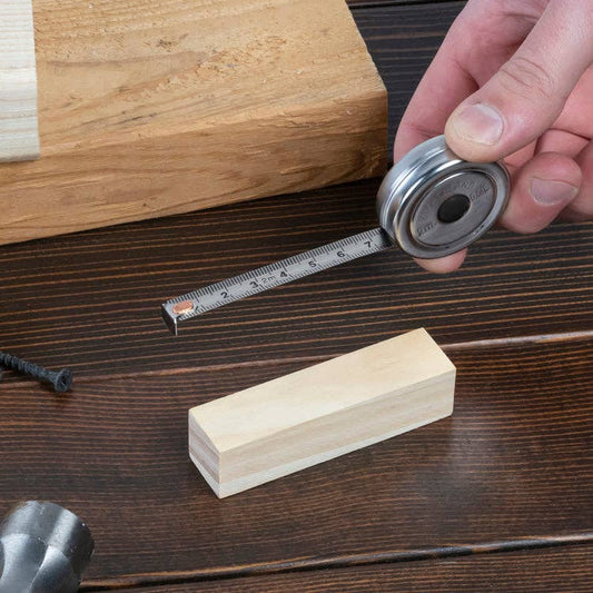 Mellow Monkey mini stainless steel retractable tape measure showing inches and centimeters on a wooden workbench