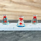 Mellow Monkey miniature glass fish inside a clear glass bag with a red tie, set of three on a stone display base.