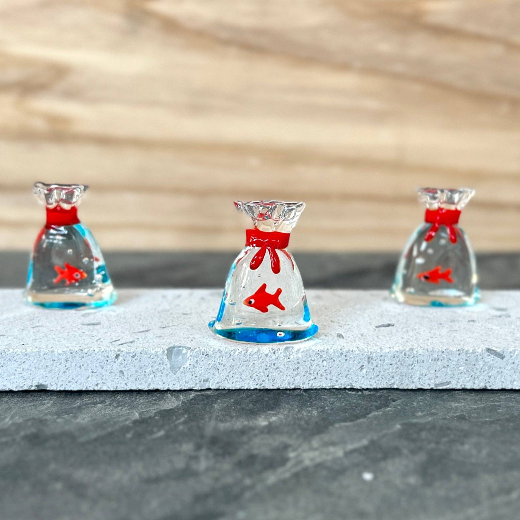 Mellow Monkey miniature glass fish inside a clear glass bag with a red tie, set of three on a stone display base.