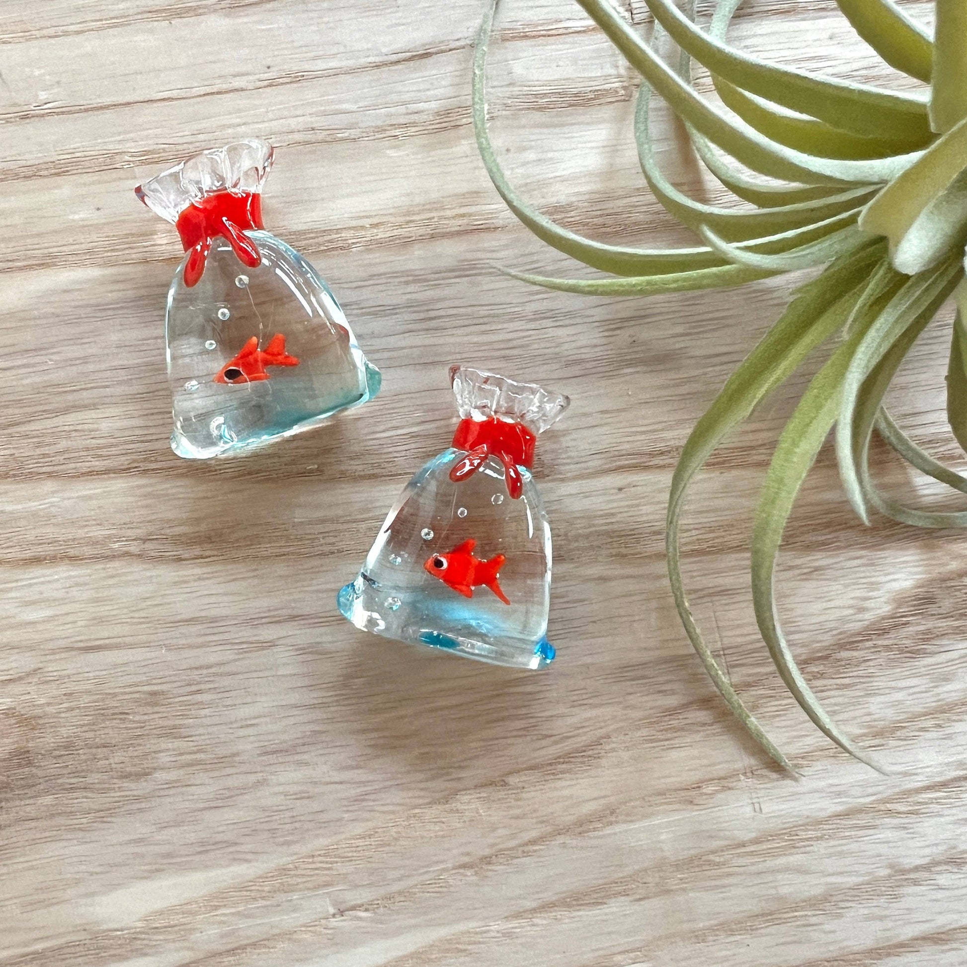 Mellow Monkey miniature glass fish inside a clear glass bag with a red tie, measuring one inch.