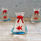 Mellow Monkey 1-inch miniature glass goldfish figurine inside a clear glass bag with a red tie on a wooden surface.