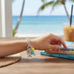 Mellow Monkey silver charm bracelet featuring mint polka dot fish and starfish charms on a beach table setting.