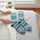 Mellow Monkey Nordic crew socks in mint and blue fair isle pattern resting on a cozy bed with hands nearby