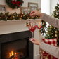 Mellow Monkey December Diamonds Mistletoe Santa merman ornament in a martini glass held by hands near a fireplace.