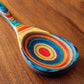 Mellow Monkey Montego Bay colorful wooden cooking spoon with teal, blue, red, orange, and yellow layered wood design.