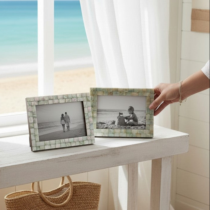 Mellow Monkey mother of pearl tile photo frames in seafoam green displayed on a white wooden table by a beach window.