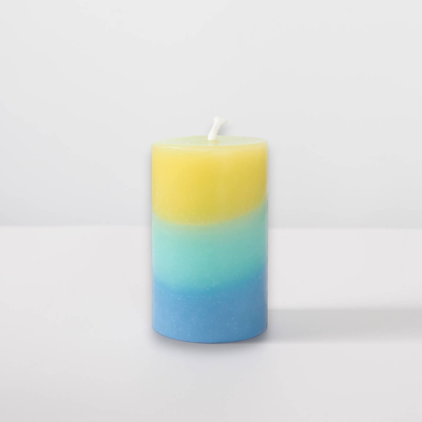 Mellow Monkey multi-scented pillar candle featuring yellow, teal, and blue wax layers with a cotton wick.