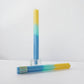 Mellow Monkey green, blue, and yellow square taper candle with three scents in a glass holder.