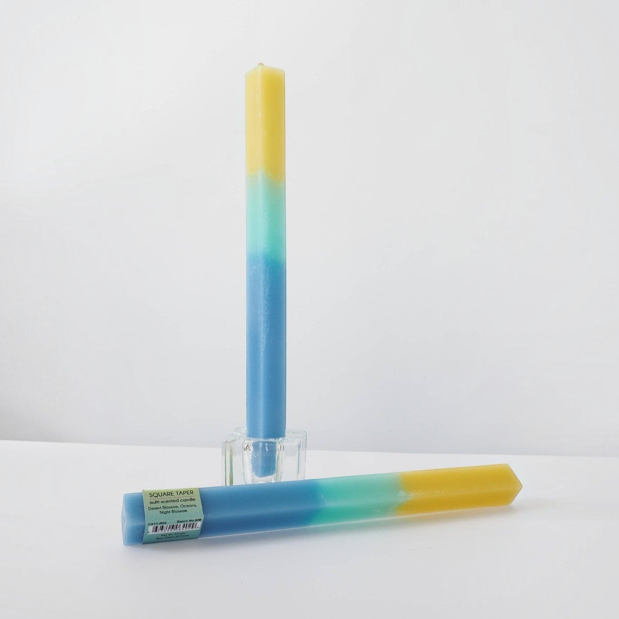 Mellow Monkey green, blue, and yellow square taper candle with three scents in a glass holder.