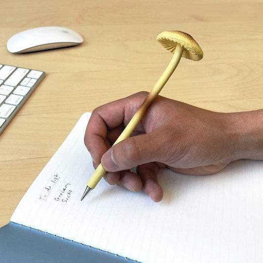 Mellow Monkey Mushroom Pen with a realistic tan cap and stem, held by a hand writing in a notebook.