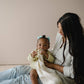 Mellow Monkey Snuggle Me natural organic cotton muslin nursing cover with built-in silicone teether held by a baby.