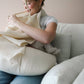 Mellow Monkey natural organic cotton muslin nursing cover with built-in teether being used by a mother on a sofa.