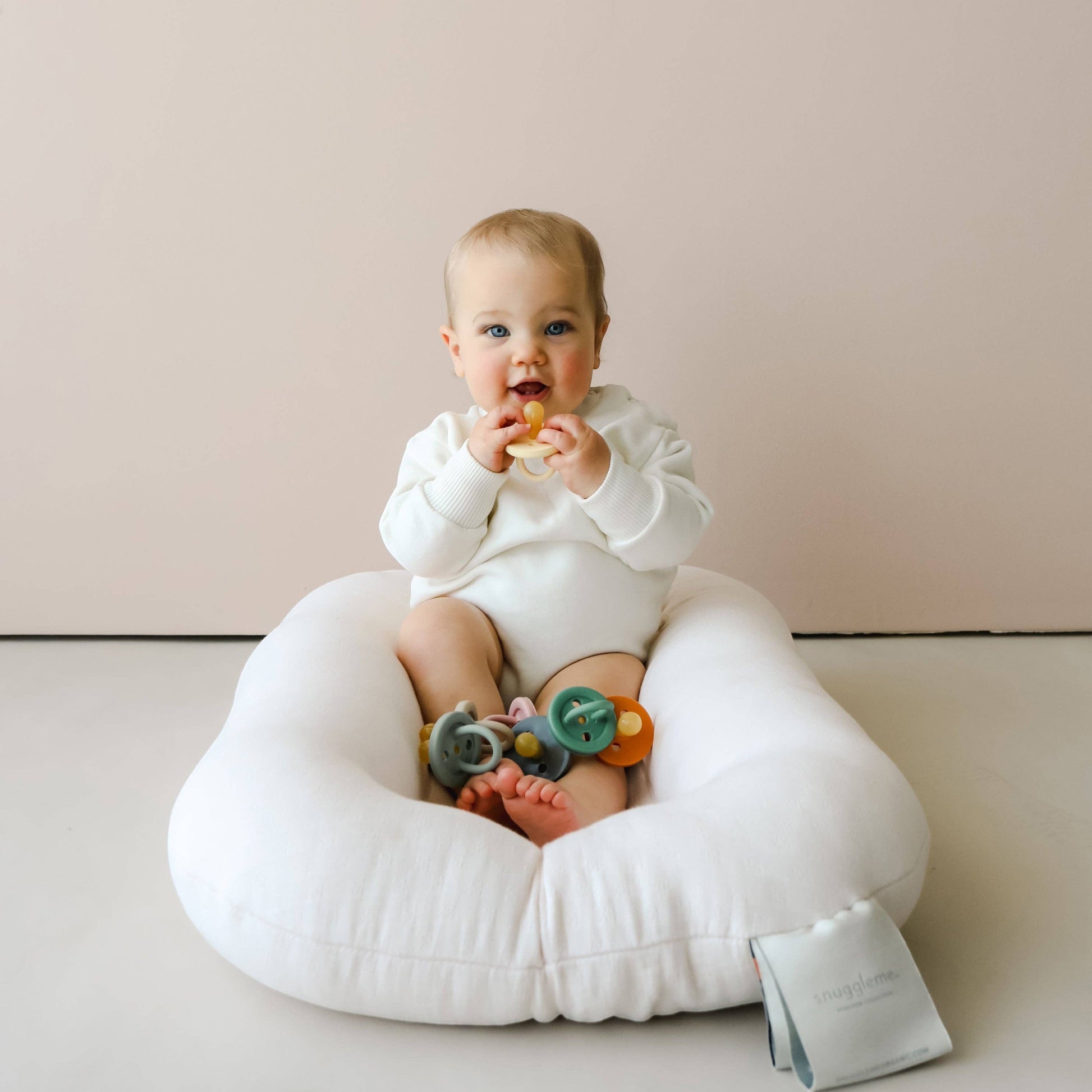 Mellow Monkey baby sitting in a white lounger holding a natural rubber Ember + Ember pacifier
