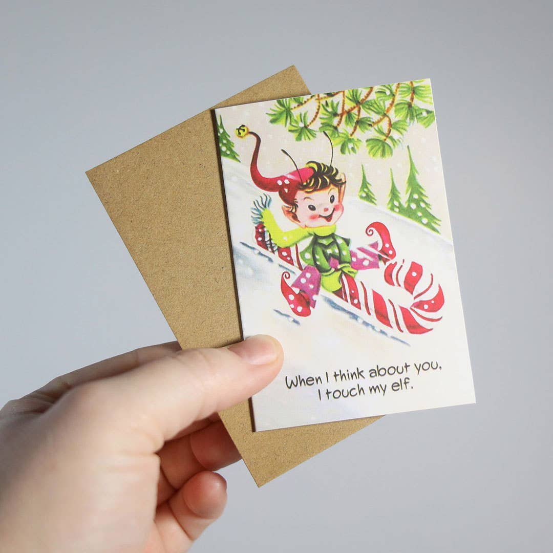 Mellow Monkey mini Christmas card with vintage elf illustration and risqué text, held with a kraft paper envelope.