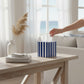 Mellow Monkey navy and white striped paper mache tissue box cover on a wooden table in a bright coastal room.