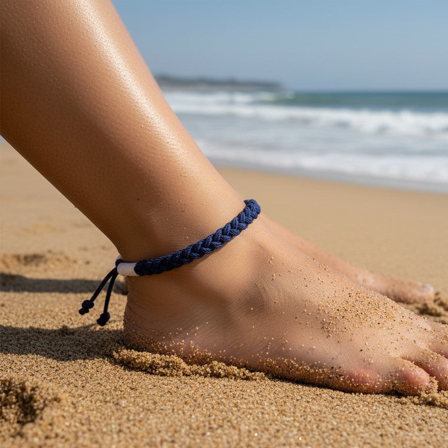 Mellow Monkey navy blue woven cotton nautical anklet worn on a person's ankle at the beach.