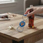 Mellow Monkey NBA New York Knicks metal bottle opener keychain being used to open a glass soda bottle on a wooden table
