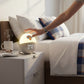 Mellow Monkey New York Knicks sunrise alarm clock on a bedside table with a hand reaching to touch the glowing light.