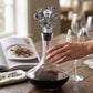 Mellow Monkey silver octopus wine bottle stopper with blue crystal accents on a glass decanter on a wooden table.