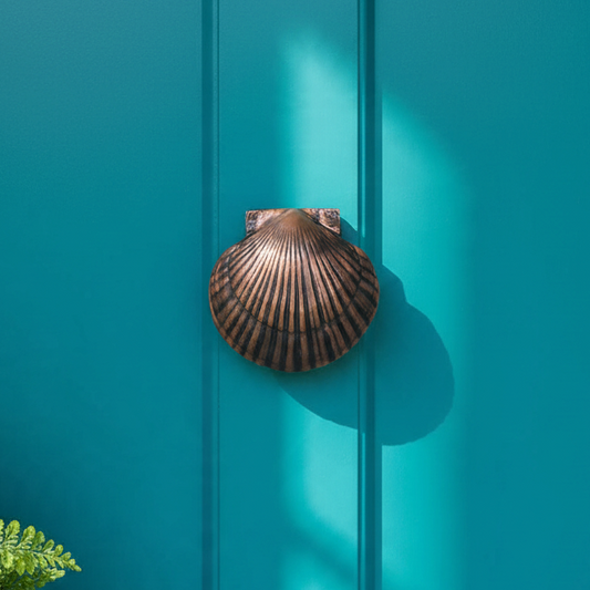Mellow Monkey oiled bronze scallop shell door knocker mounted on a vibrant teal front door with brass hardware.