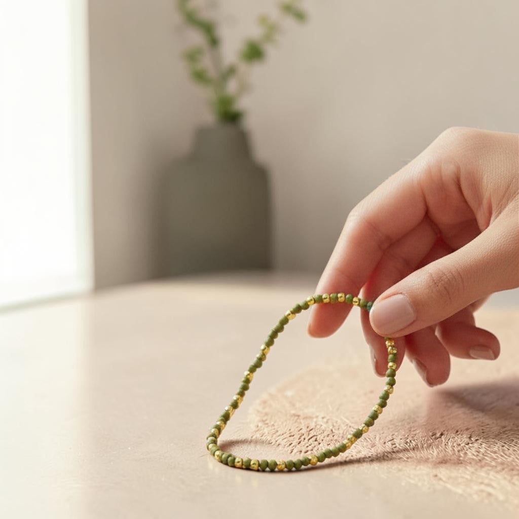 Mellow Monkey olive seed bead bracelet with 18K gold plated brass accents held by a hand on a wooden table.