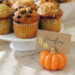 Mellow Monkey orange pumpkin place card holder with a gold-embellished card in front of a tray of muffins