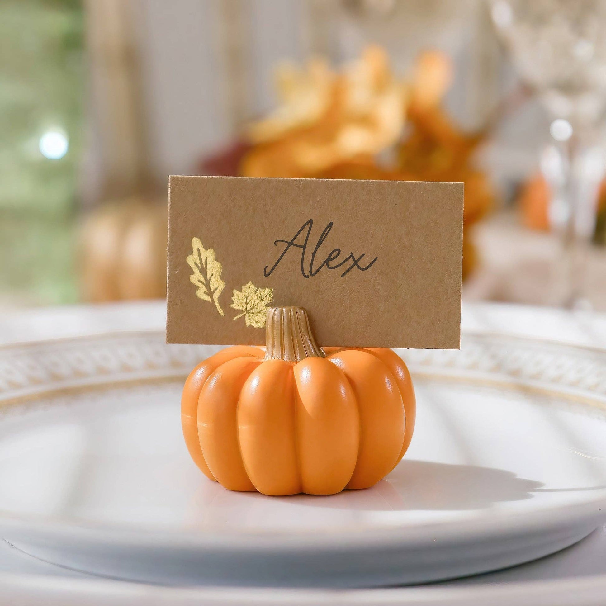 Mellow Monkey orange pumpkin place card holder with gold-embellished card on a white dinner plate for Thanksgiving