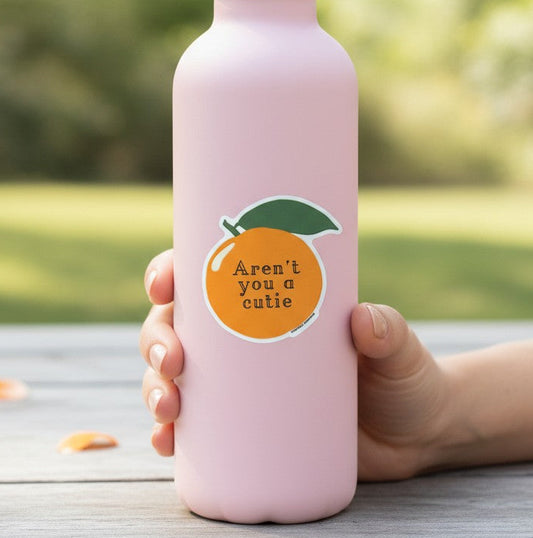 Mellow Monkey Aren't You A Cutie vinyl orange sticker on a light pink water bottle held by a hand outdoors