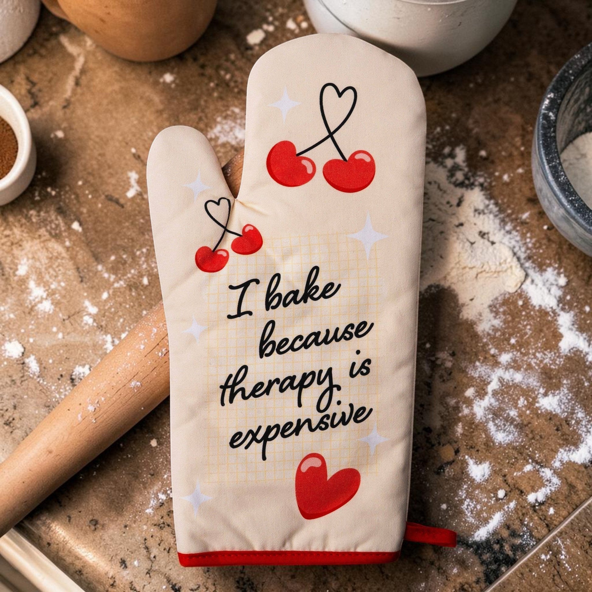 Mellow Monkey cream oven mitt with red trim, featuring cherries and the text "I bake because therapy is expensive."