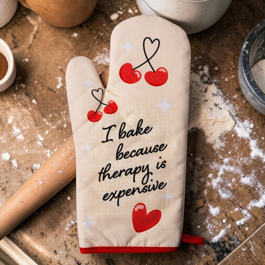 Mellow Monkey cream oven mitt with red trim, featuring cherries and the text "I bake because therapy is expensive."