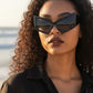 Woman with curly hair wearing Mellow Monkey oversized black cat eye sunglasses with UV400 protection at the beach.