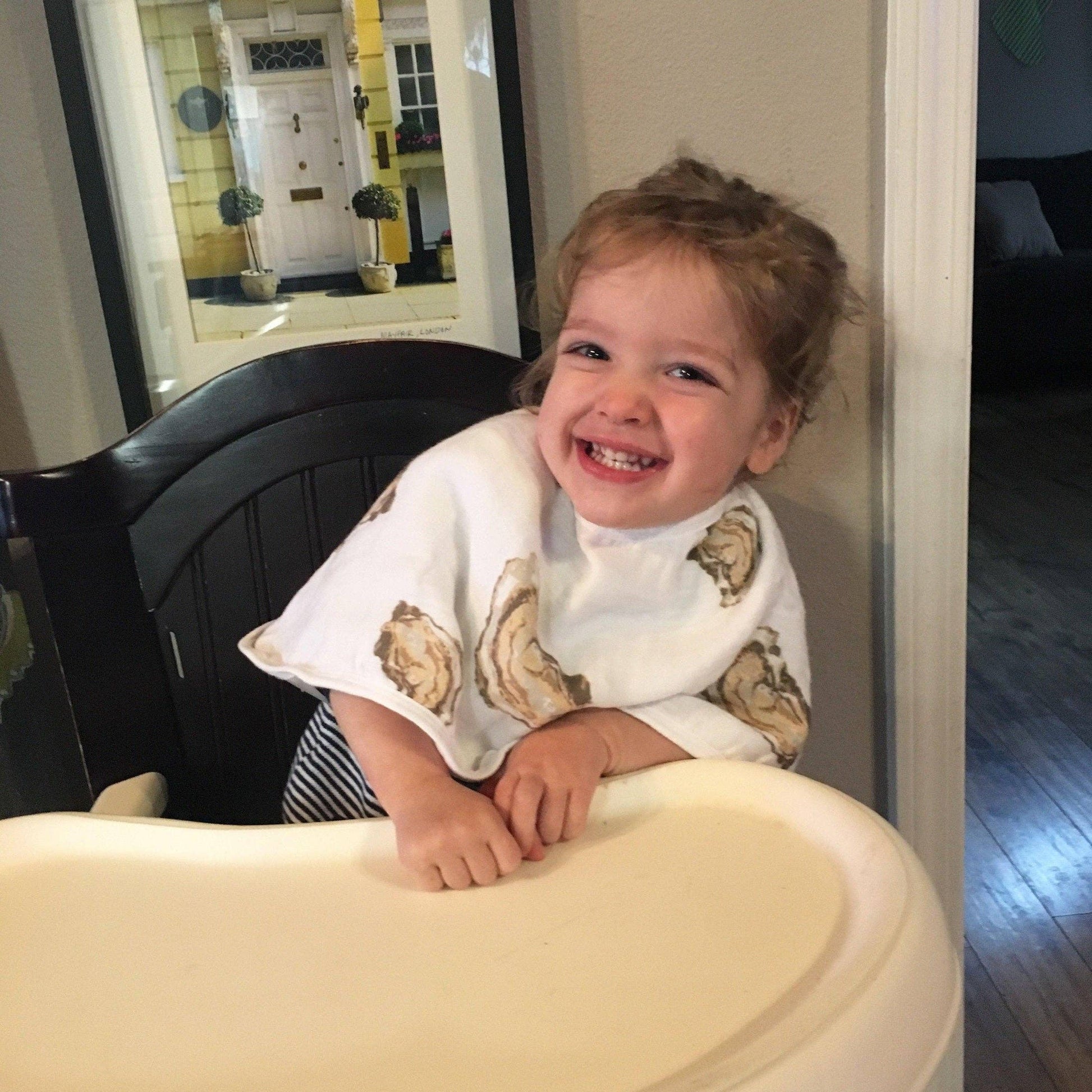 Mellow Monkey oyster print 2-in-1 bamboo and cotton muslin baby bib worn by a smiling toddler in a high chair