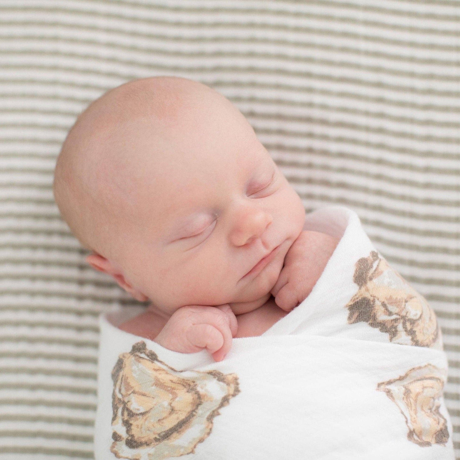 Mellow Monkey baby swaddled in a soft white muslin blanket featuring an oyster shell print