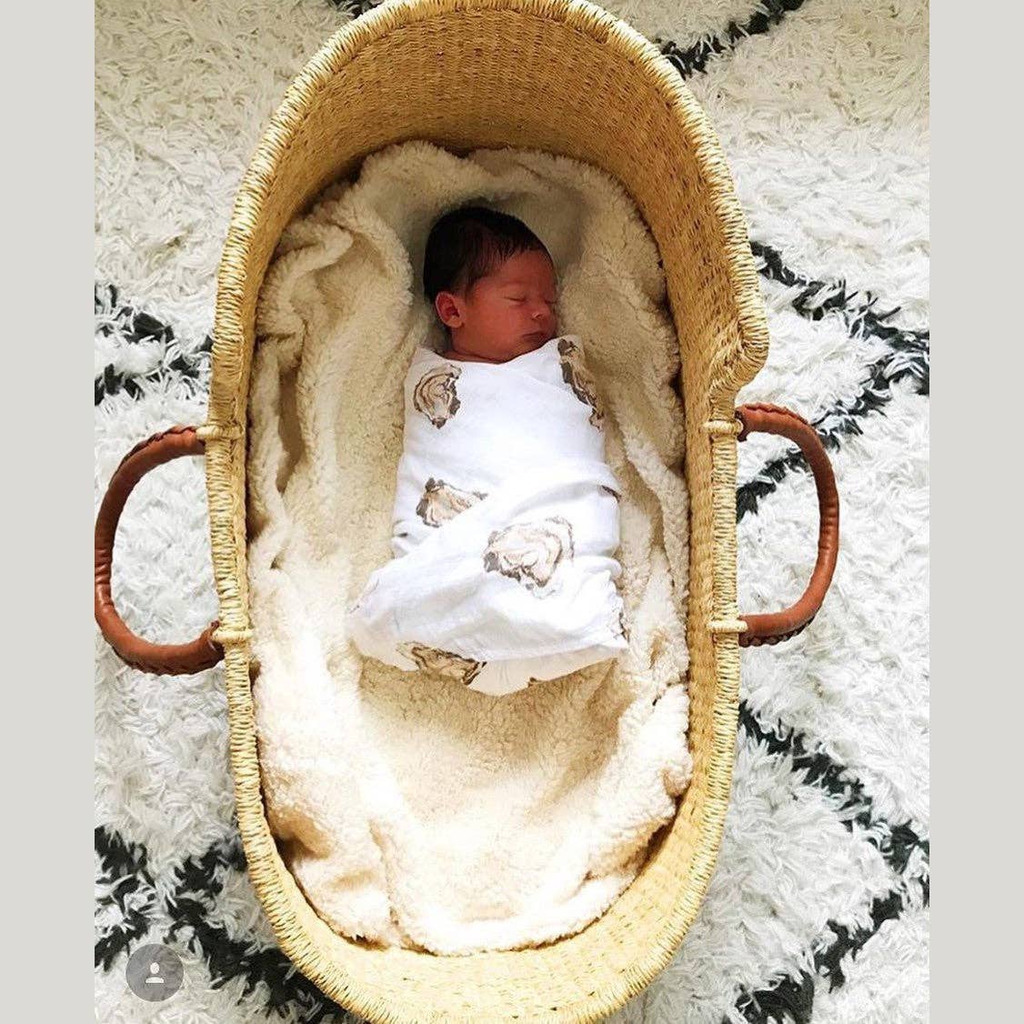 Mellow Monkey oyster print muslin swaddle blanket wrapped around a newborn baby in a woven moses basket