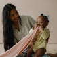 Mellow Monkey Petal nursing cover in soft pink organic muslin being used by a baby with a built-in silicone teether.