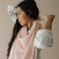 Mellow Monkey Petal nursing cover in soft pink organic cotton muslin worn by a woman adjusting the neckline