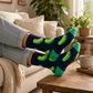 Mellow Monkey bamboo knit socks with green dill pickle pattern on black background, worn by person on cozy sofa.