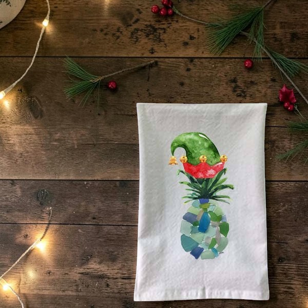 Mellow Monkey flour sack towel featuring a festive sea glass pineapple wearing a green and red elf hat