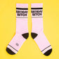 Mellow Monkey pink gym crew socks with Birthday Bitch text, black heels and toes, and gold glitter stripe accents.