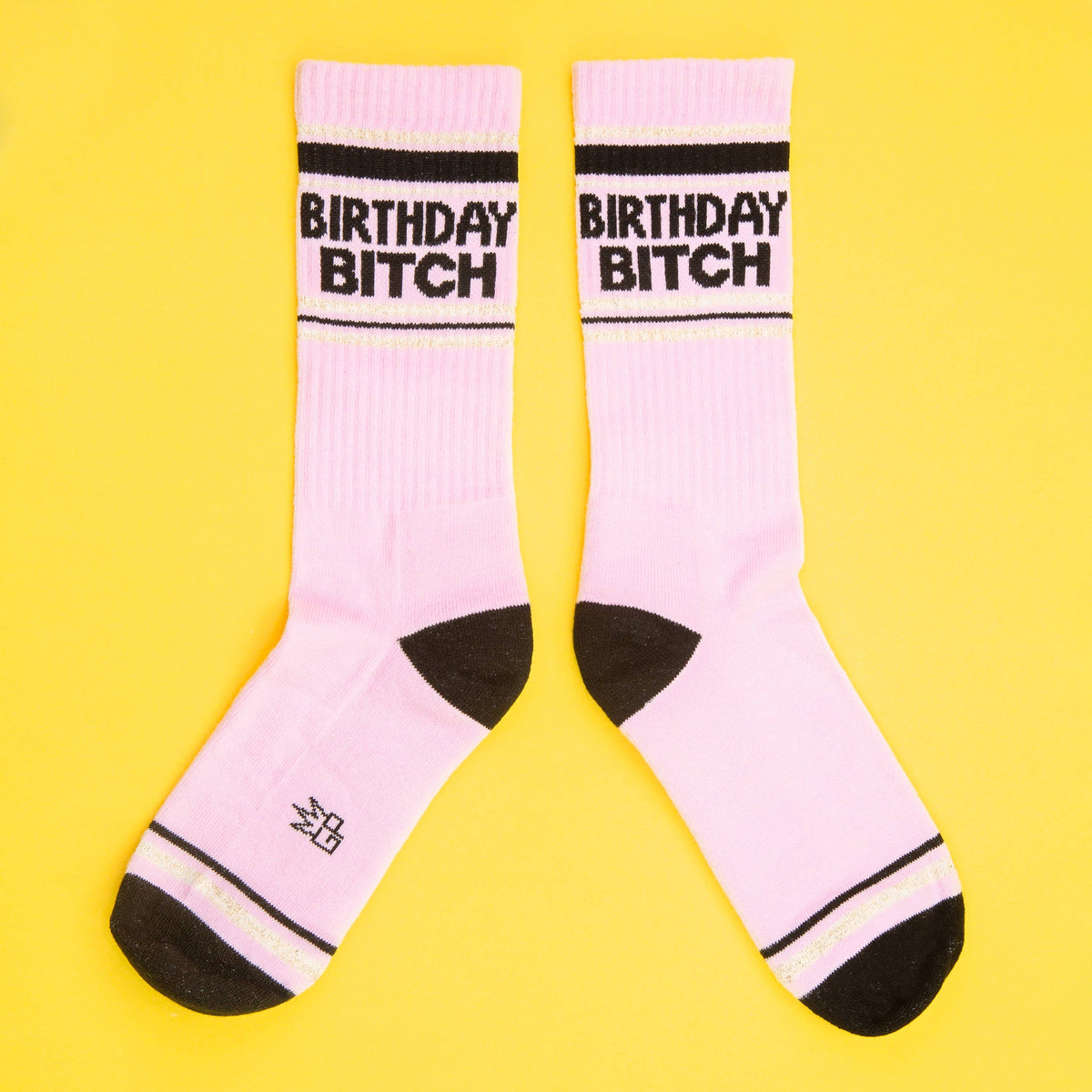 Mellow Monkey pink gym crew socks with Birthday Bitch text, black heels and toes, and gold glitter stripe accents.
