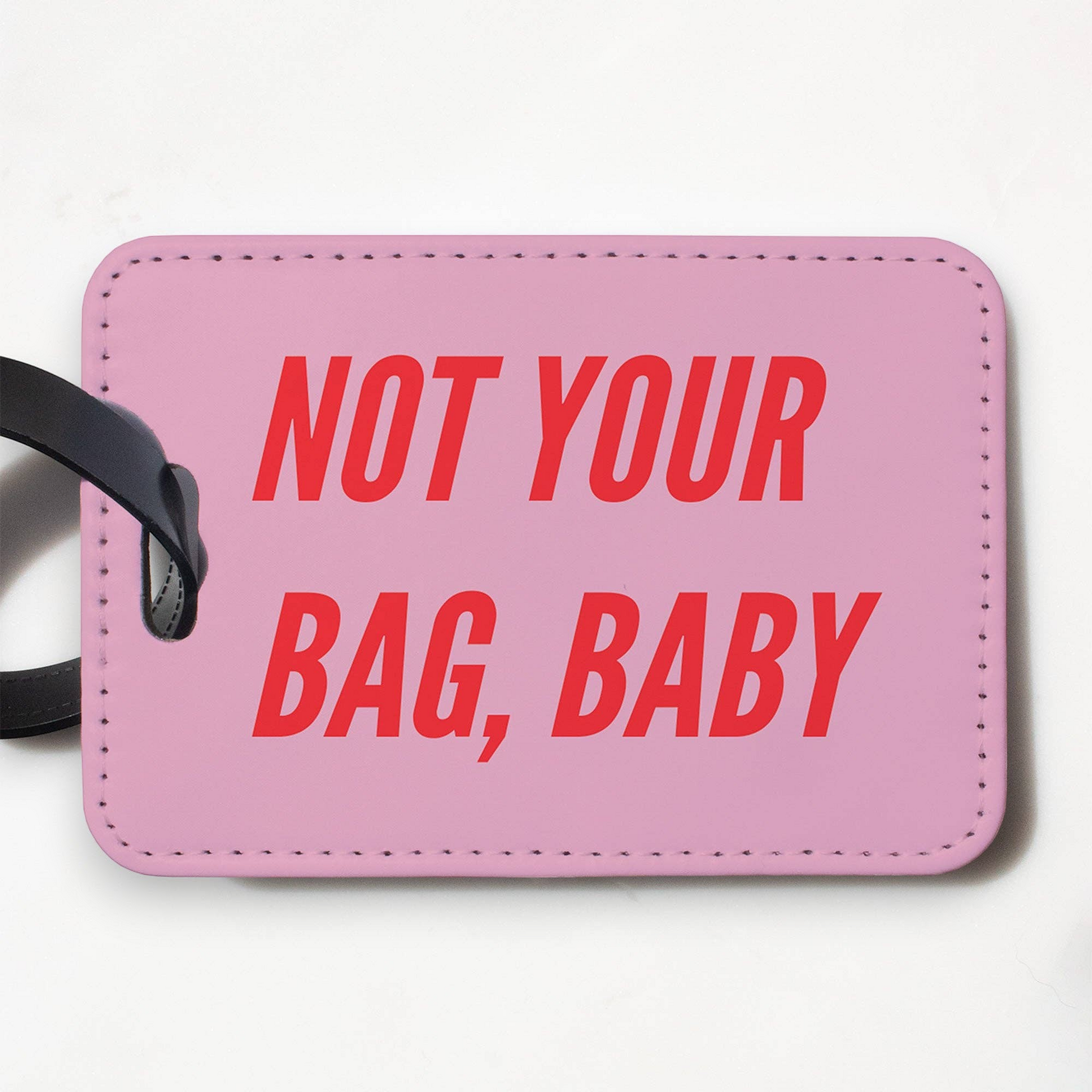 Mellow Monkey pink faux leather luggage tag with Not Your Bag Baby text in red and a black plastic strap